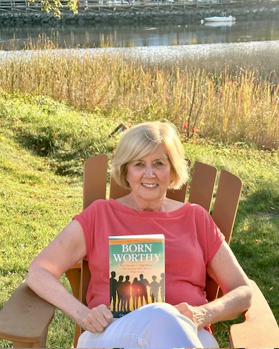 Gail outdoors by the water holding her book Born Worthy